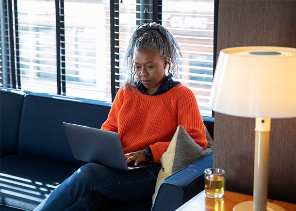 A woman sits on a couch typing on a laptop