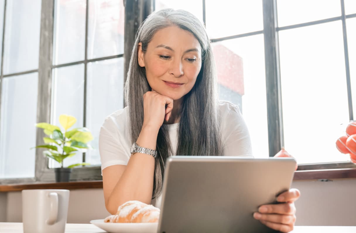 Woman at a table with breakfast looking at a tablet.