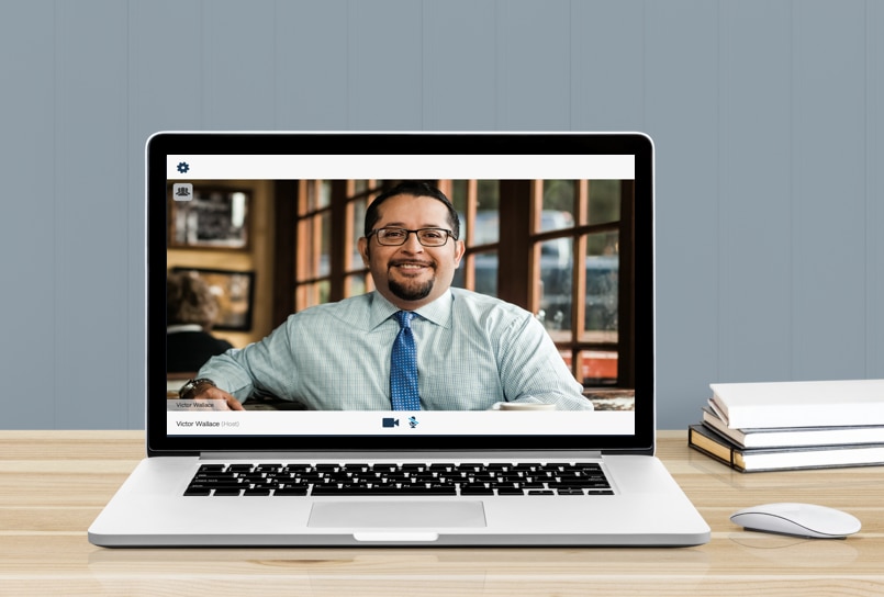 Image of a man on a laptop screen. The laptop is on a desk.