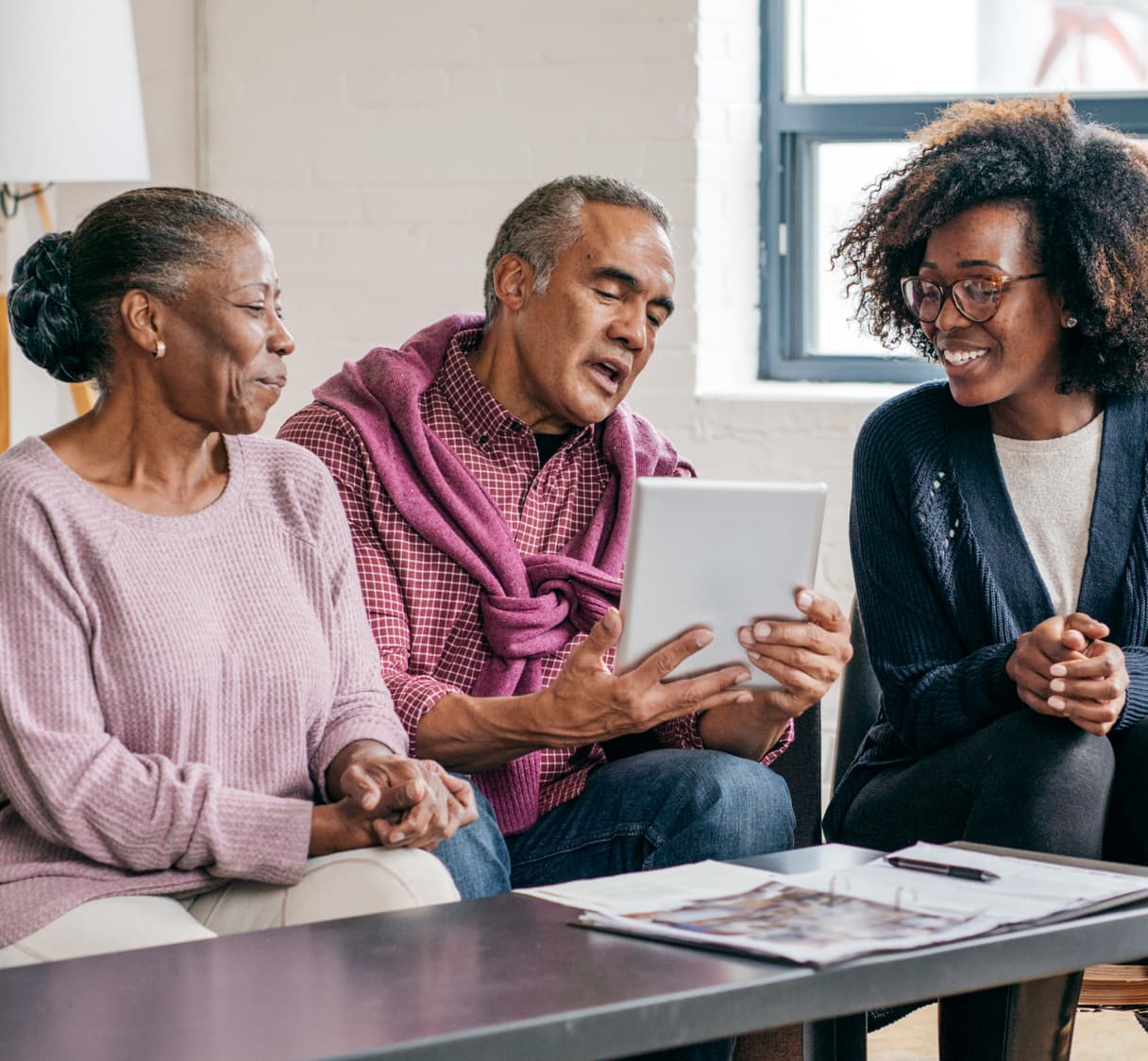 A couple sits next to a woman, with the man holding a tablet.