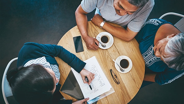 Aerial view of three people at a table reviewing documents and drinking coffee