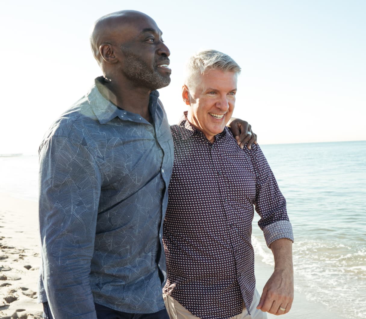 Two smiling men walking down the beach with an arm around each other