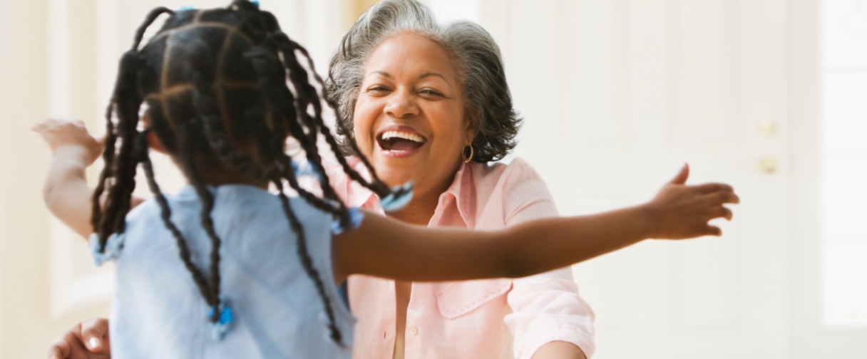 A small child running into the open arms of a smiling grandmother figure.